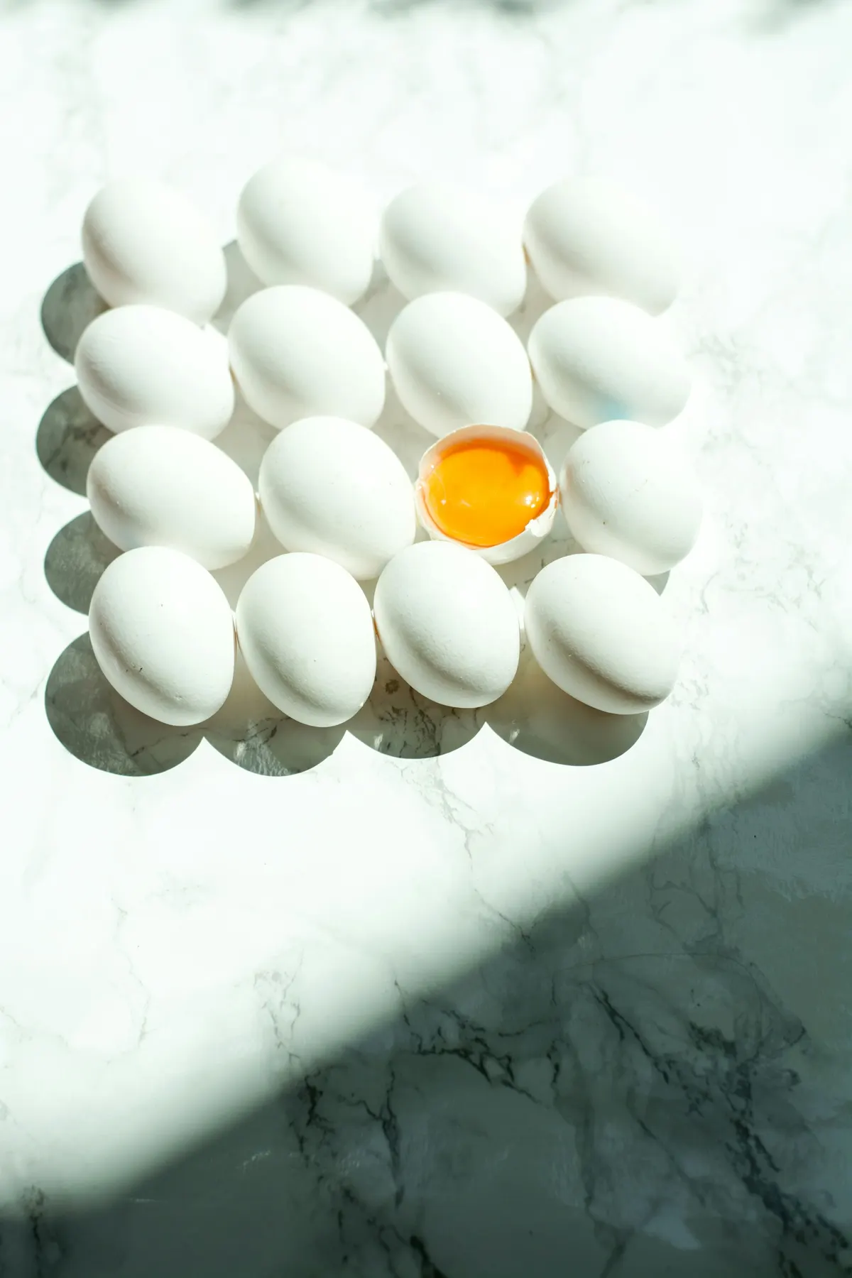 Maple de huevos blancos visto desde arriba, con un huevo abierto mostrando la yema al centro